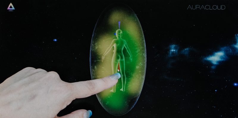 Aura imaging screen showing a full body energy portrait in green and gold, with a fingertip touching the display