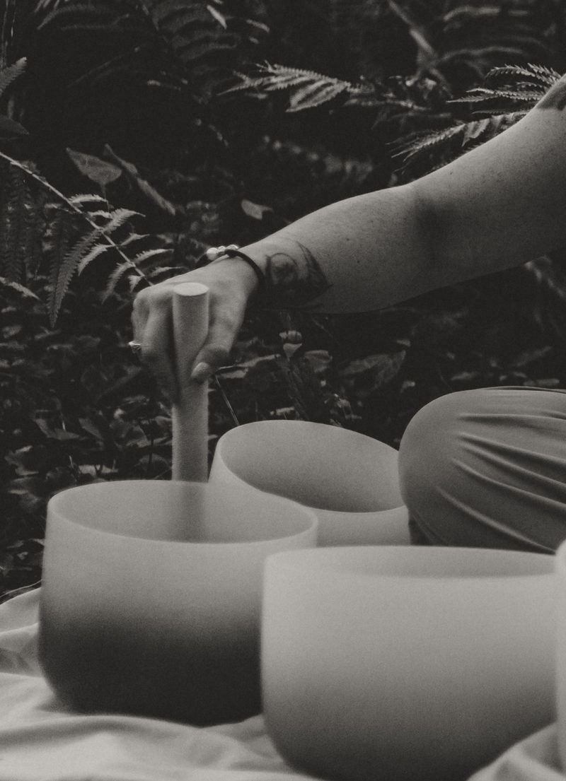 Black and white close view of a mallet resting inside one bowl in a cluster of crystal singing bowls