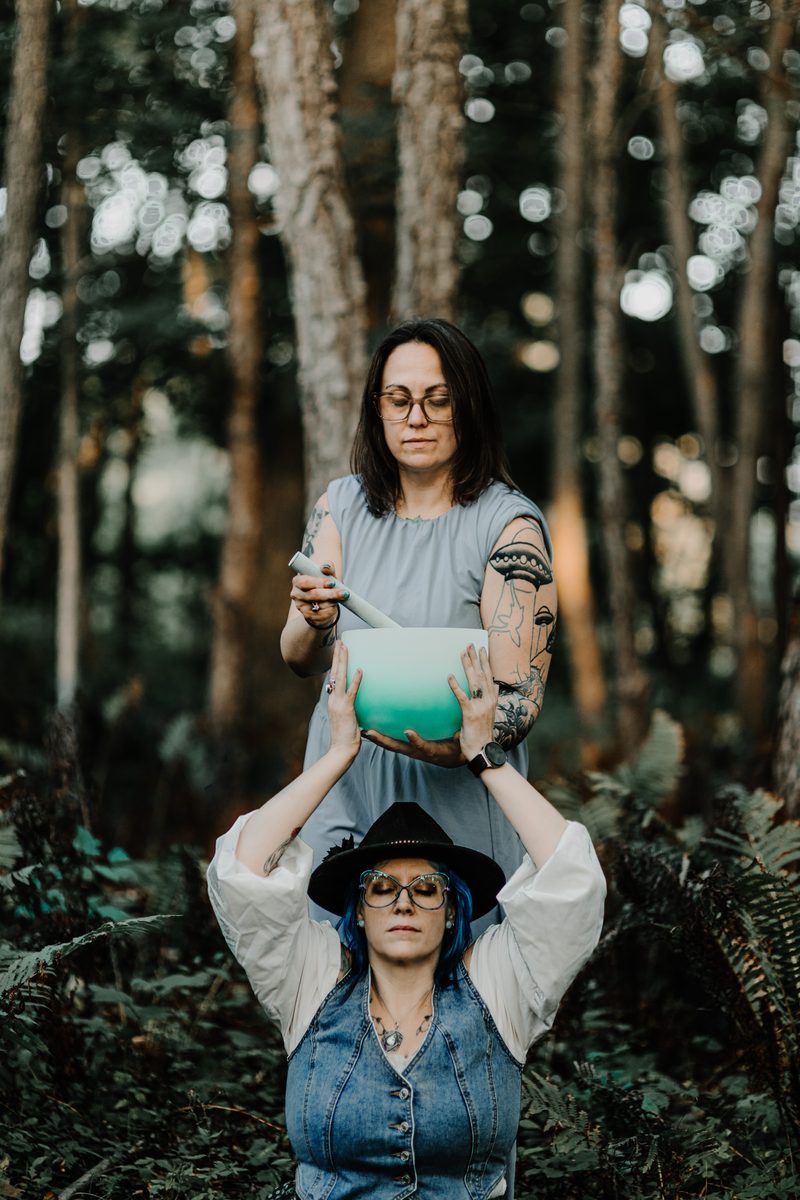 Mallory Bey plays a crystal singing bowl above a seated client wearing a wide brimmed hat