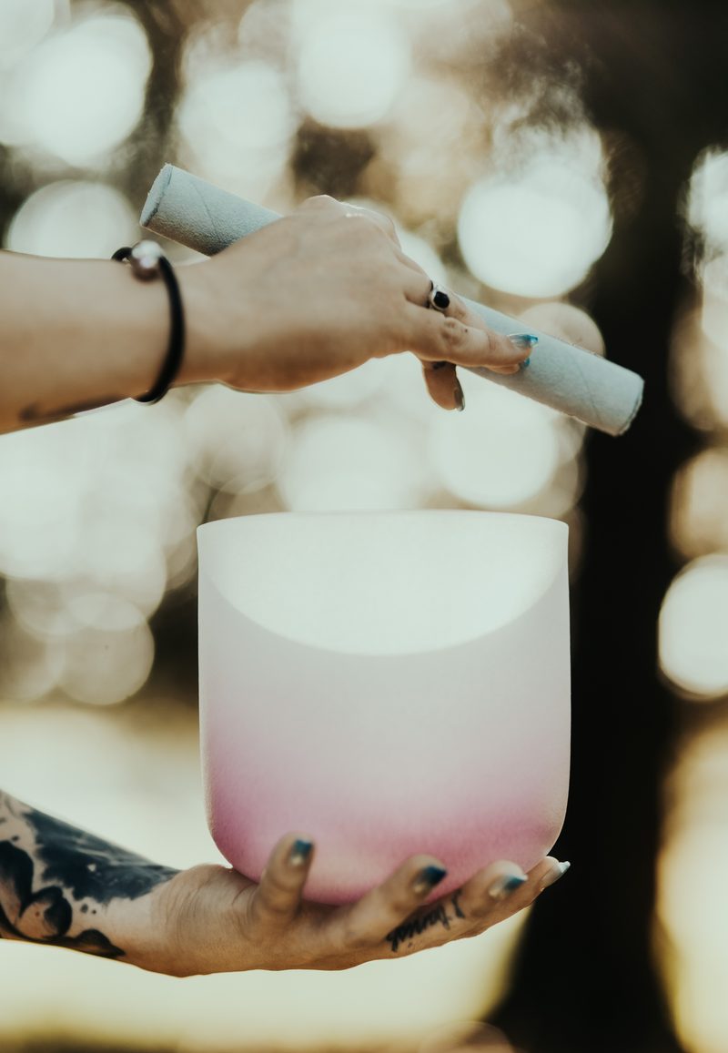 Close view of a hand and mallet at the rim of a pink and white crystal singing bowl in soft light