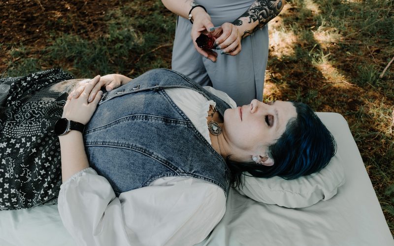 A client rests on the treatment table outdoors while Mallory Bey works above her