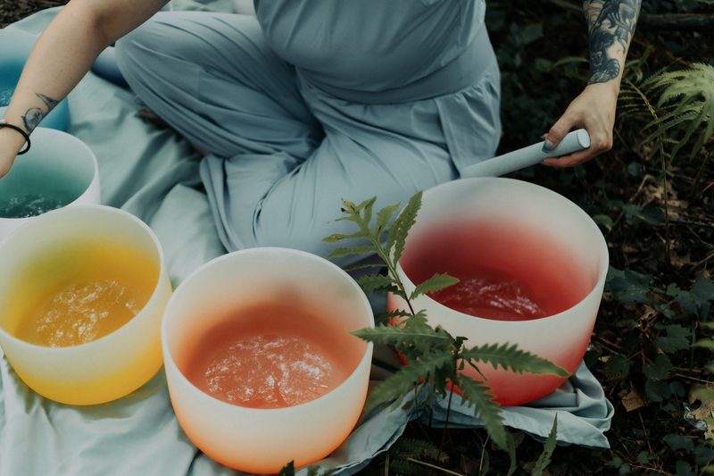 Three crystal singing bowls in yellow, peach and red resting on a pale blue cloth with a fern frond