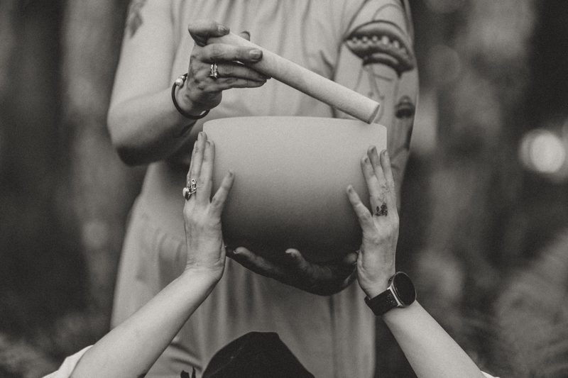 Black and white photograph of two pairs of hands cradling a crystal singing bowl while a mallet rests at the rim