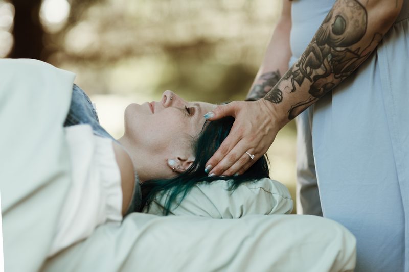 Mallory Bey cradles a reclining client's head with both hands during an outdoor session